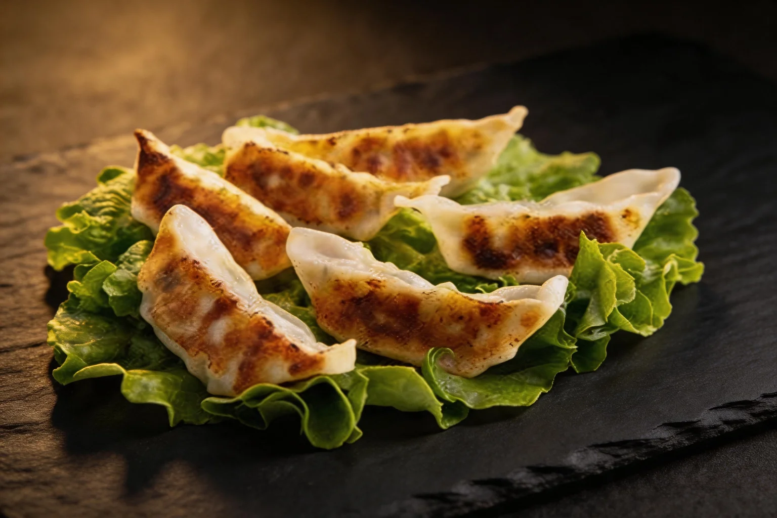Six golden gyoza on a bed of lettuce, dark stone background