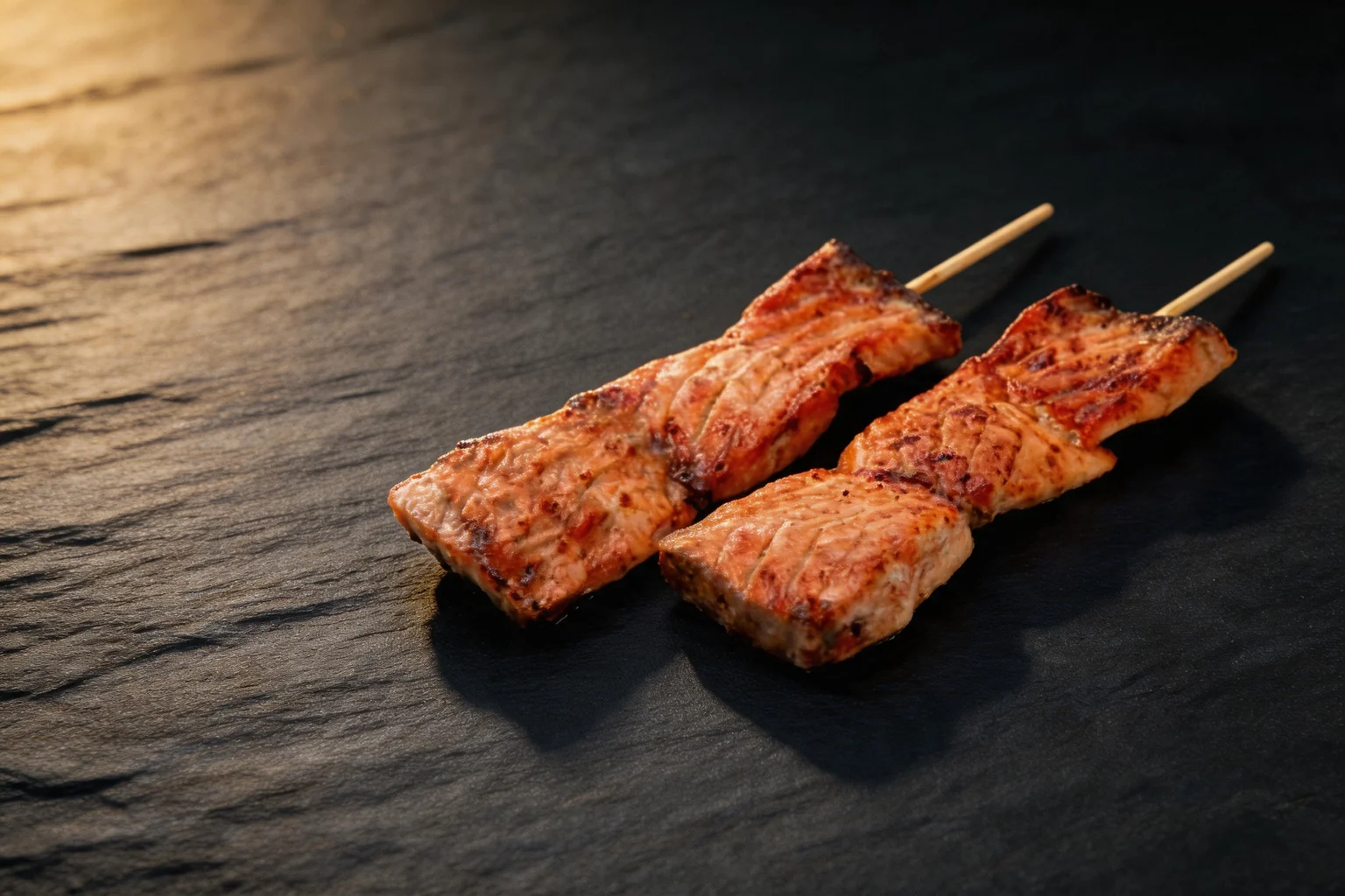 Two grilled salmon skewers, dark stone background
